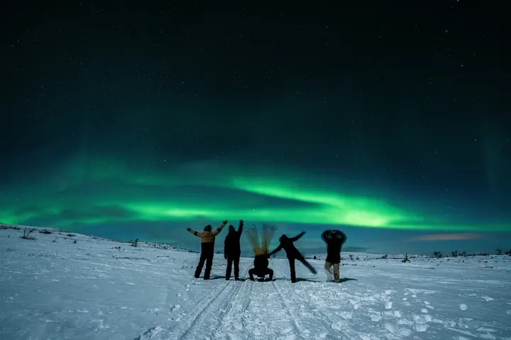 A small group celebrating in the snow under the northern lights